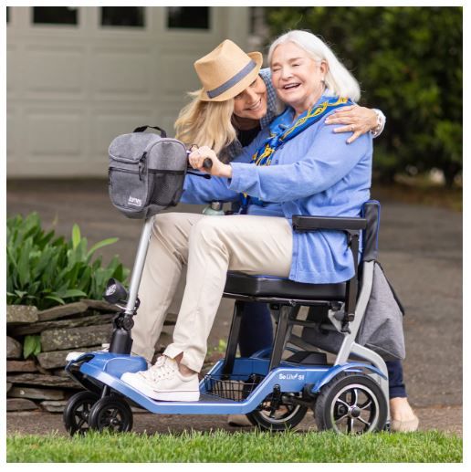 Young Woman (Standing) Hugging Older Woman (Sitting on Scooter)