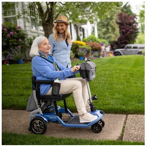 Young Woman Walking Beside Older Woman Riding Scooter Down Sidewalk