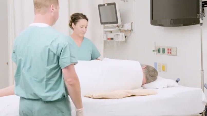 2 nurses positioning a Z-Flow beneath a patient who is turned on his side