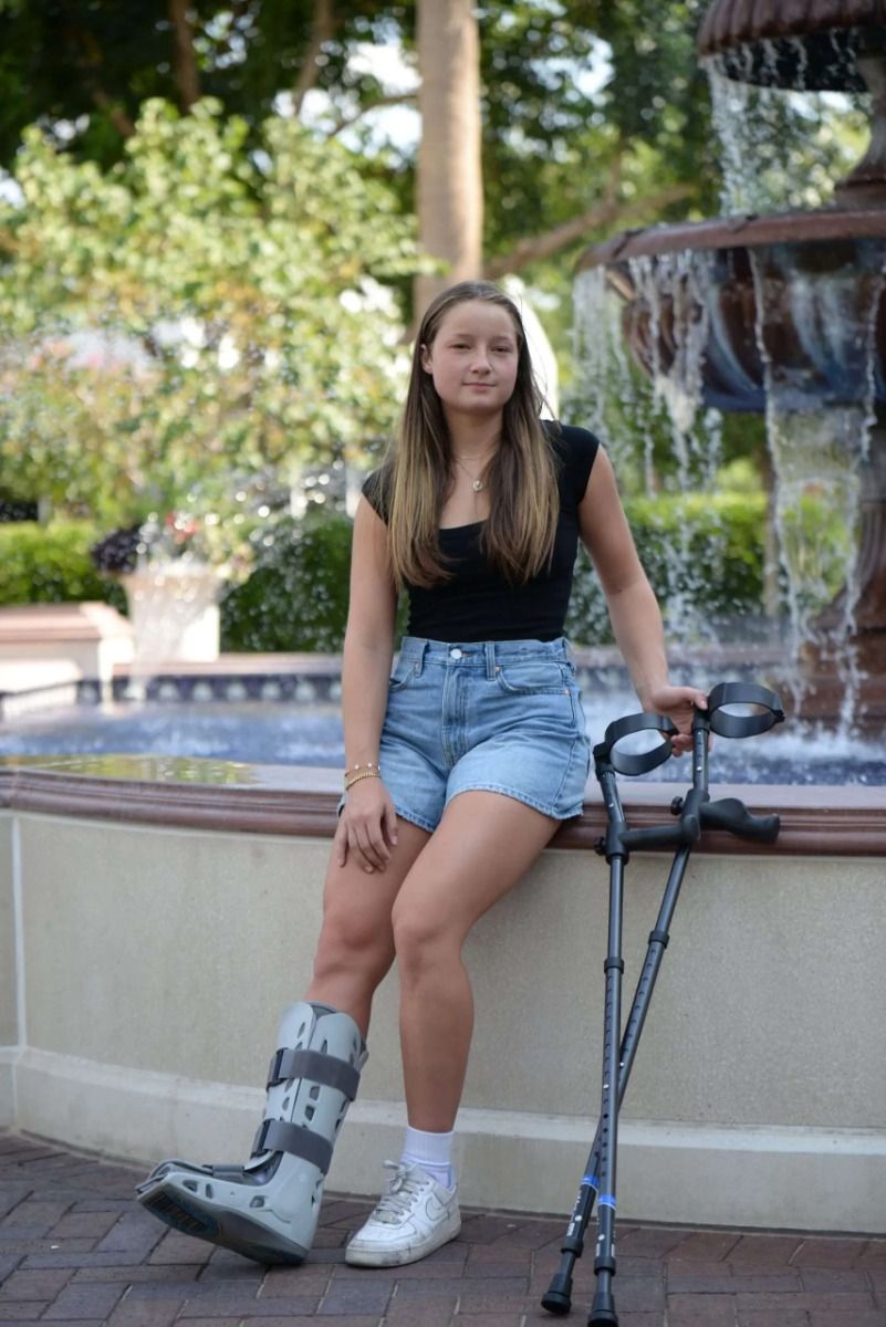 Woman sitting on a park fountain's edge with forearm crutches