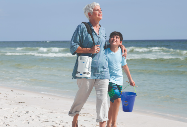 A patient walking on the beach using a portable concentrator.