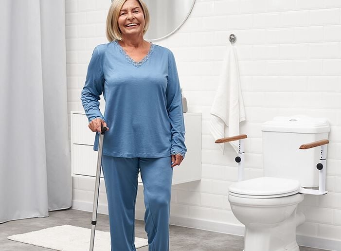 Woman Standing With Cane Beside Toilet Safety Rails