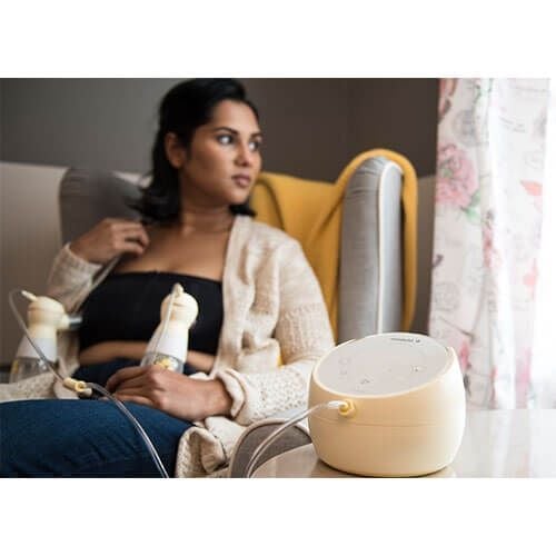 A mother uses the Sonata Double Breast Pump while comfortably seated in an armchair.
