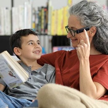 A grandmother reads to her grandson using the OrCam MyEye attached to her glasses.