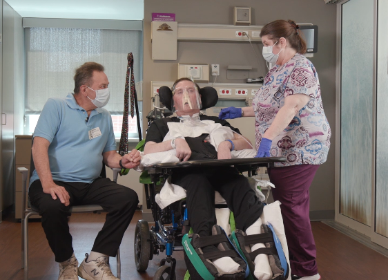 A patient using the Shiley Flexible Adult Tracheostomy Tube with caregivers by his side