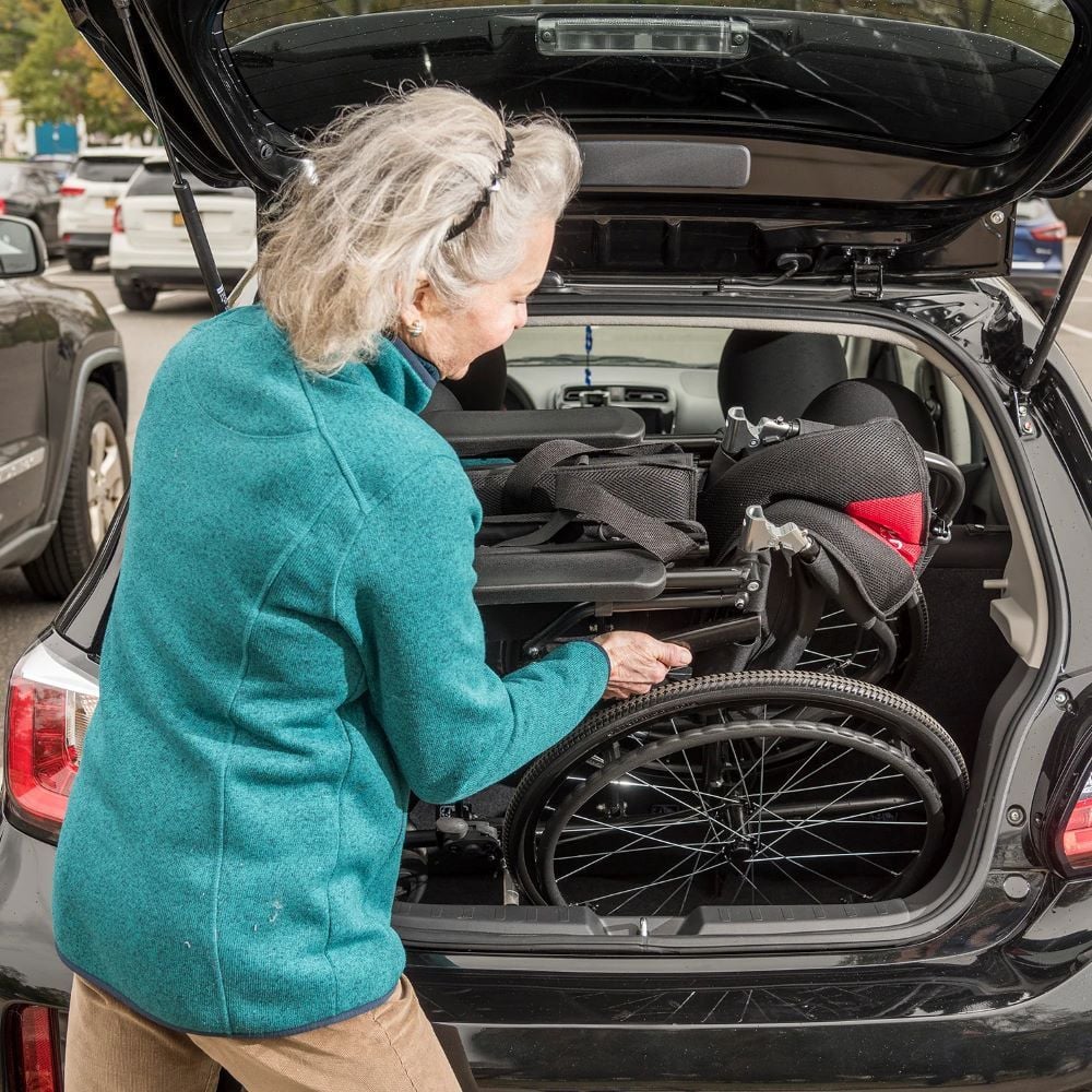 Woman lifting So Lite Super Lightweight wheelchair into car trunk
