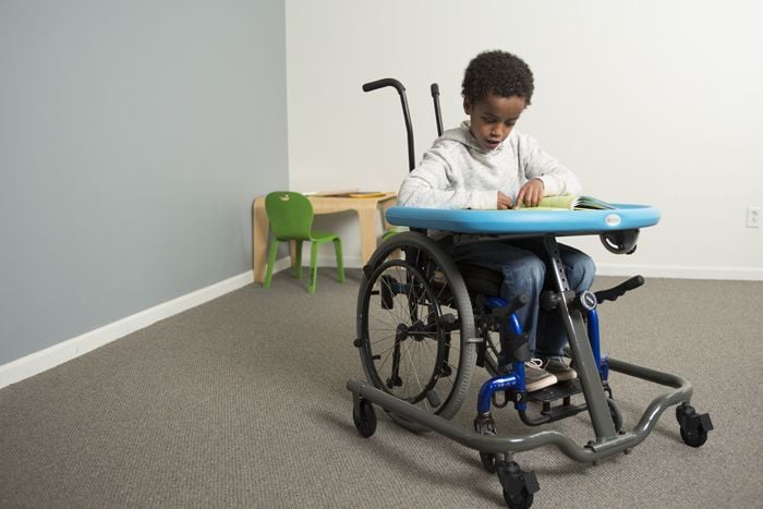 Little boy in wheelchair reads a book on activity tray