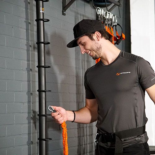 Trainer hooks orange spine strap to wall-mounted spine bar