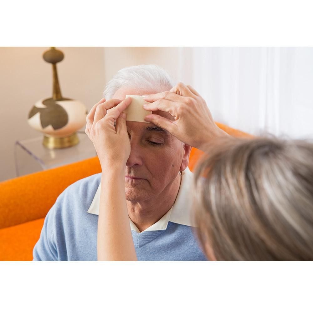 Caregiver applies ManukaHD dressing to older man's forehead