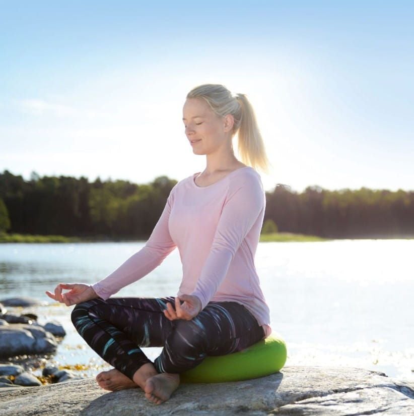 Woman Sitting Cross Legged on a Yoga Relax Cushion Near a Lake