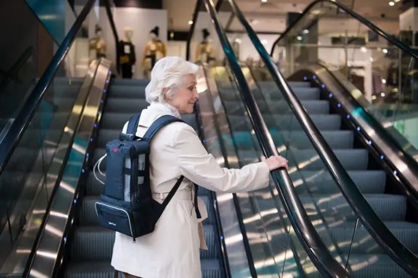 A woman riding the escalator while carrying a portable oxygen concentrator in a rucksack
