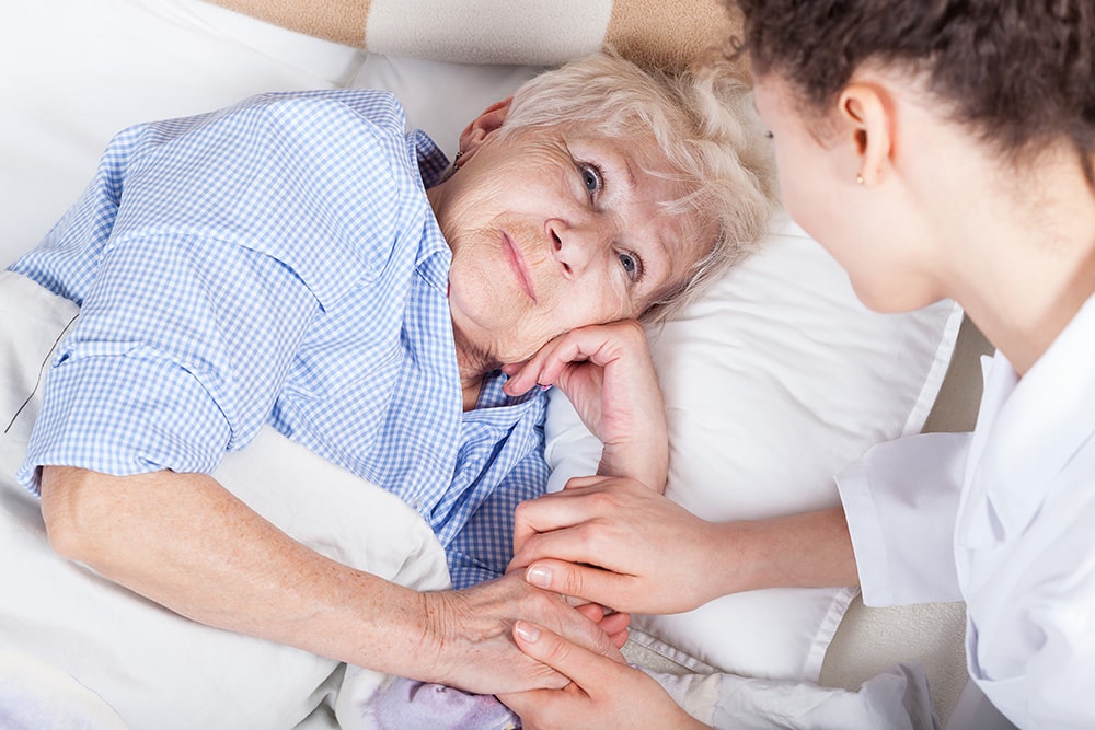 Young woman sitting with and holding the hand of an elderly woman