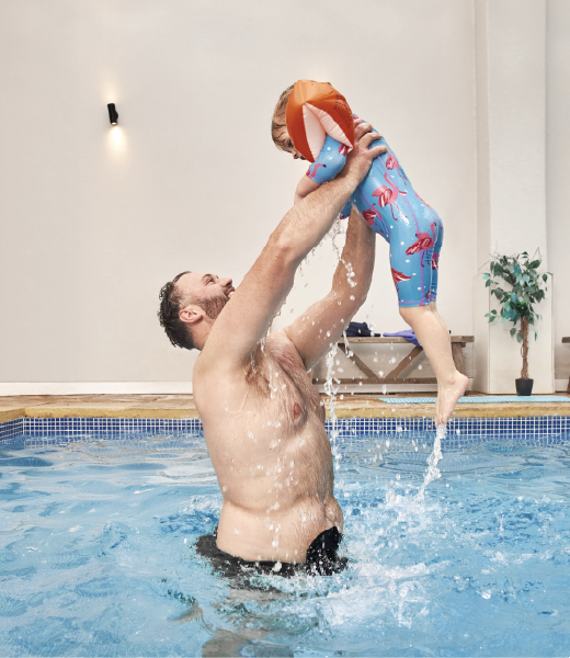 Man wearing black ostomy pouch playing with his daughter in the pool