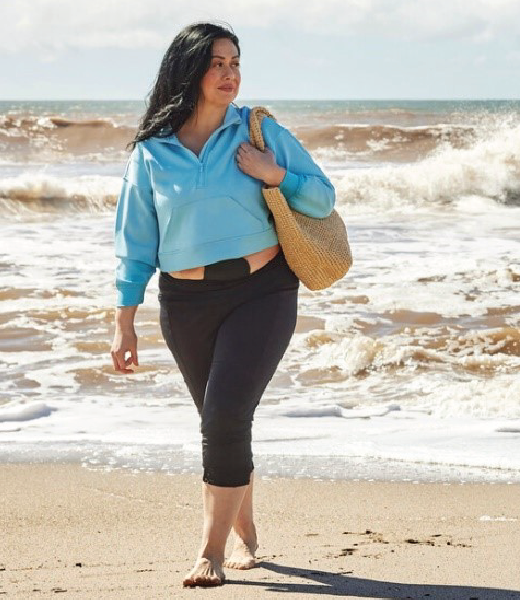Woman walking on the beach with black ostomy pouch visible