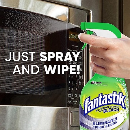 data-element= A person sprays Fantastik cleaner on the microwave