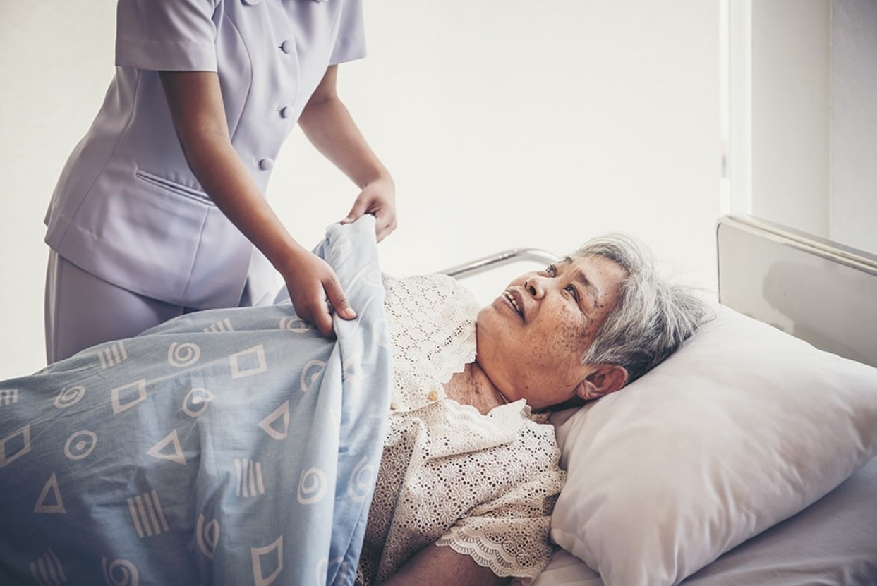 Caretaker tends to an elderly patient in a hospital bed